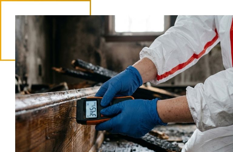 Close-up of a technician's gloved hands using a digital moisture meter to check for hidden water damage after a fire.