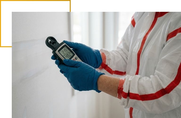 Close-up of a technician's gloved hands using a digital thermo-hygrometer to verify safe humidity levels after water damage repairs.