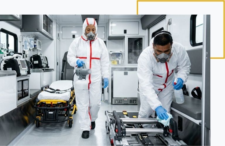 Two biohazard remediation specialists in hazmat suits utilizing advanced fogging equipment to sanitize the patient compartment of an unmarked ambulance.