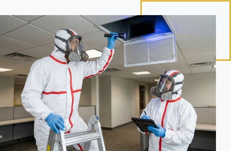 Two certified technicians inspecting commercial HVAC ceiling vents to locate and eliminate the source of airborne odors.