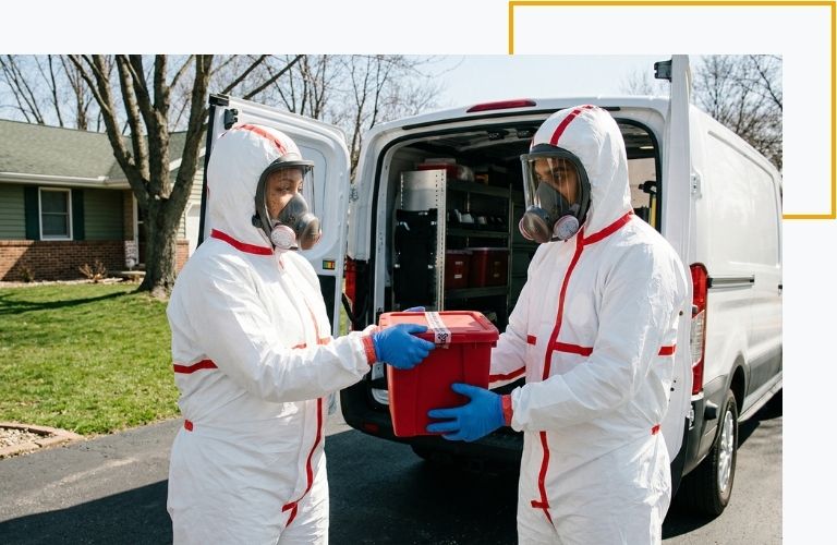 Two forensic cleanup specialists safely transferring a secure medical waste container into a transport van.